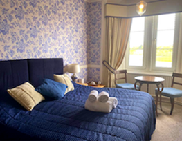 Bed with blue bedcover and headboard with window behind.