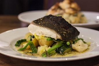 A plate with a fillet of white fish served on green vegetables.