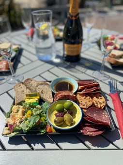 Rectangilar meat platter on a grey slatted wooden table with wine and glasses blurred in the background.