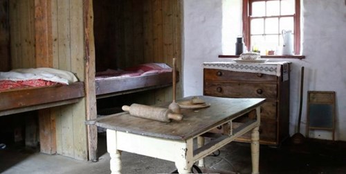 Interior of historic Scottish house showing a table with rolling pin in the foreground and two recessed beds on the left.