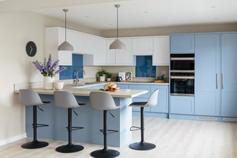 Bright kitchen with pale blue units and breakfast bar with four black and grey hight stools.